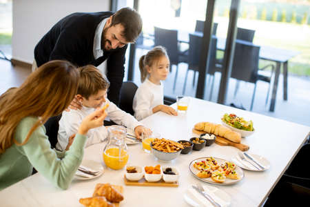 Young happy family talking while having breakfast at dining table at apartmentの写真素材