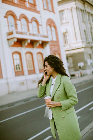 Pretty young woman using smartphone on the street and holding takeaway coffee