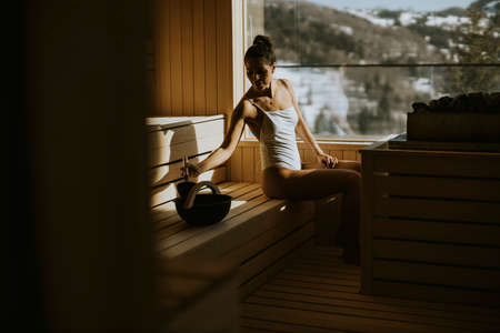 Attractive young woman pouring water onto hot stone in the saunaの写真素材