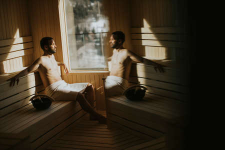 Handsome young man relaxing in the sauna and watching winter forest through the windowの写真素材