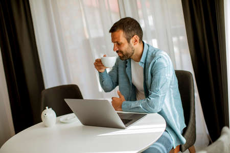 Handsome young man using laptop and drink tea in the living roomの写真素材