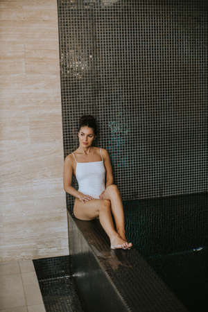 Pretty young woman relaxing on the poolside of indoor swimming poolの写真素材