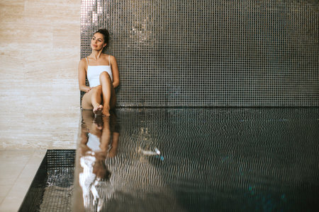 Pretty young woman relaxing on the poolside of indoor swimming poolの写真素材