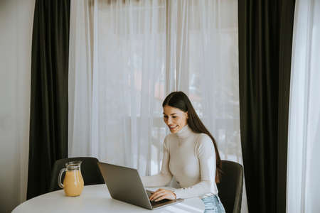 Young woman using a laptop computer and drinking healthy orange juice in the roomの写真素材