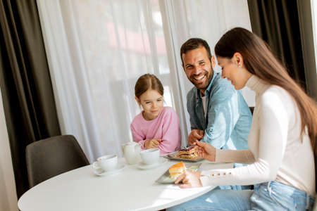 Happy young famila eat cakes and drink tea together in the roomの写真素材