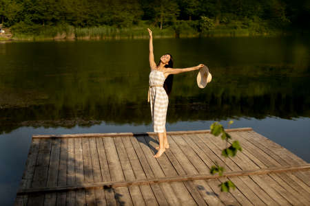 Happy young woman standing on the wooden pier at the calm lake on a hot summer dayの写真素材