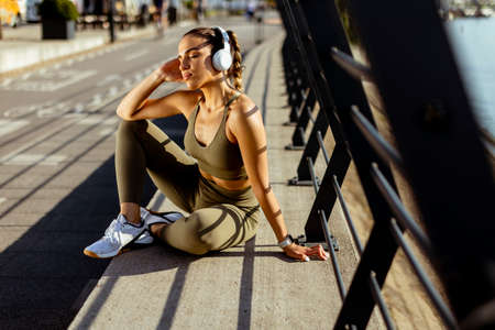 Pretty young woman with earphones takes a break after running in the urban areaの写真素材