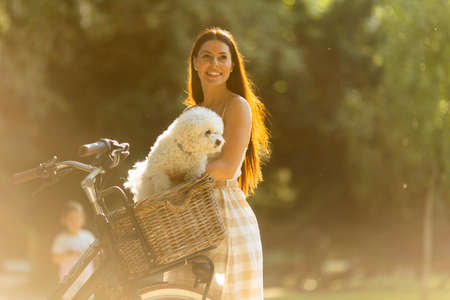 Pretty young woman with white bichon frise dog in the basket of electric bikeの写真素材