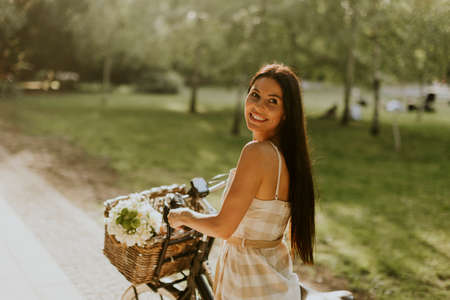 Pretty young woman with flowers in the basket of electric bikeの写真素材