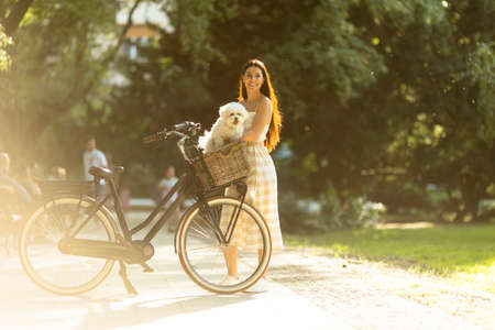 Pretty young woman with white bichon frise dog in the basket of electric bike