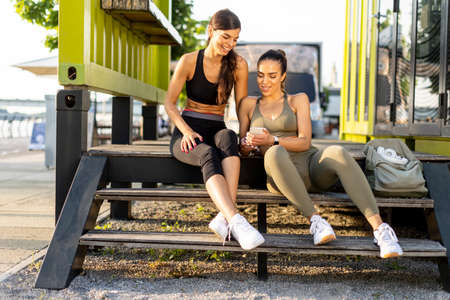 Pretty young women in sportswear looking at mobile phone after exercise training