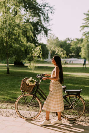 Pretty young woman with flowers in the basket of electric bikeの写真素材