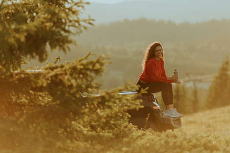 Pretty young woman relaxing on a terrain vehicle hood at countrysideの写真素材