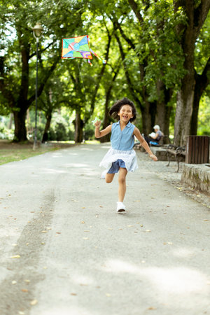 Cute little girl running happily with a kite in the parkの写真素材