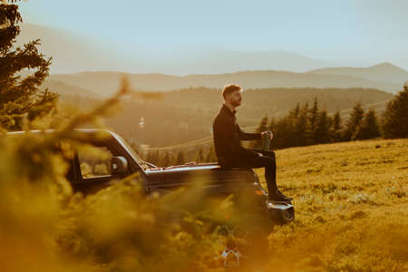 Handsome young man relaxing on a terrain vehicle hood at countrysideの写真素材
