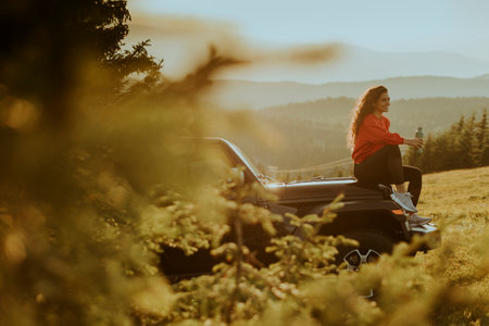 Pretty young woman relaxing on a terrain vehicle hood at countryside