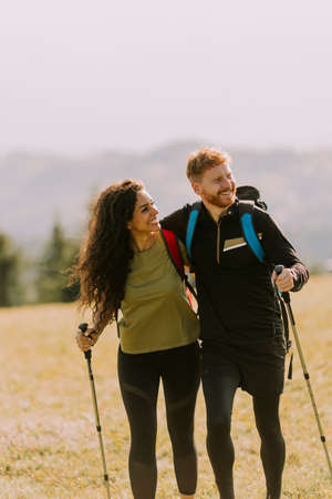 Smiling young couple walking with backpacks over green hillsの写真素材