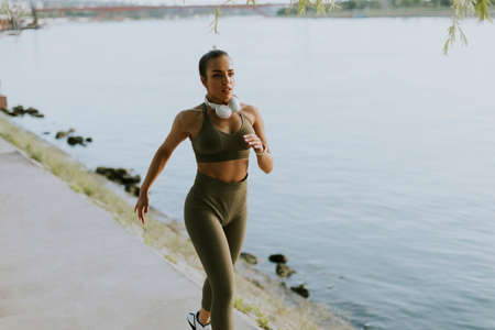 View at active young beautiful woman running on the promenade along the riverside