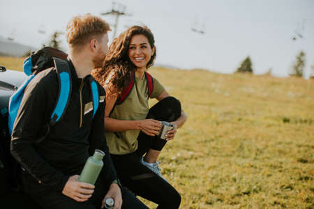 Handsome young couple relaxing on a terrain vehicle hood at countrysideの写真素材