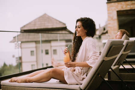 Handsome young couple relaxing on beds and drinking fresh orange juice on the outdoor terraceの写真素材