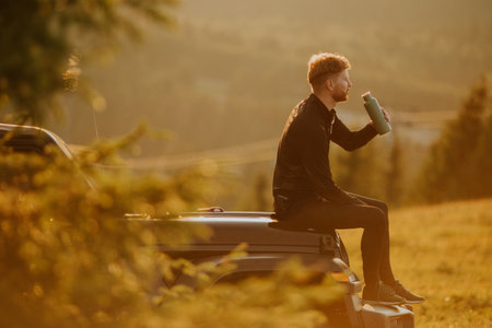Handsome young man relaxing on a terrain vehicle hood at countryside