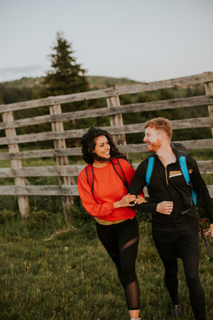 Smiling young couple walking with backpacks over green hills