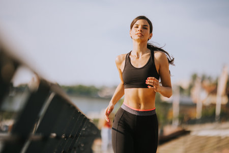 View at active young beautiful woman running on the promenade along the riverside