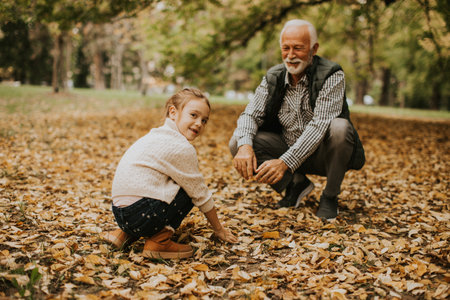 Handsome grandfather spending time with his granddaughter in park on autumn dayの写真素材