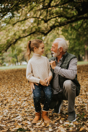 Handsome grandfather spending time with his granddaughter in park on autumn dayの写真素材