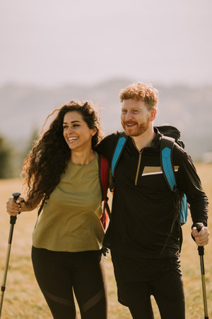 Smiling young couple walking with backpacks over green hillsの写真素材