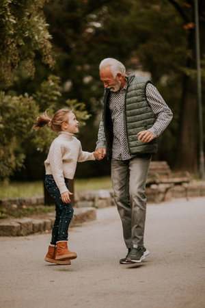Handsome grandfather spending time with his granddaughter in park on autumn dayの写真素材