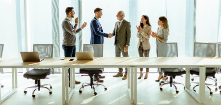 Business partners handshaking in the office after making agreement with employees near by