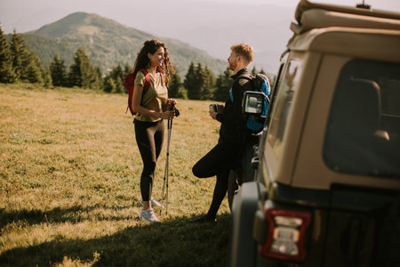 Smiling young couple preparing hiking adventure with backpacks by terrain vehicleの写真素材