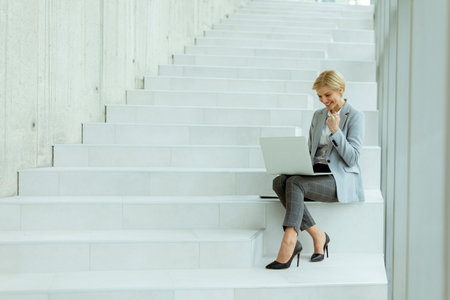 Businesswoman working on laptop on the modern office stairsの写真素材