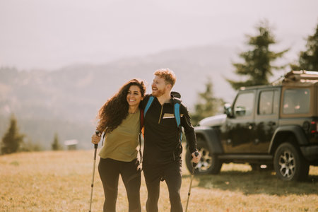Smiling young couple starting walking with backpacks over green hills