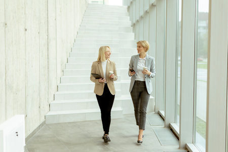 Two business women walking with digital tablet and mobile phone in the office corridor
