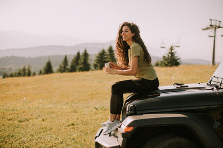 Pretty young woman relaxing on a terrain vehicle hood at countryside