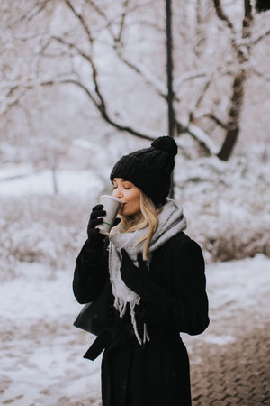 Pretty young woman n warm clothes enjoying in snow with takeaway coffee cupの写真素材