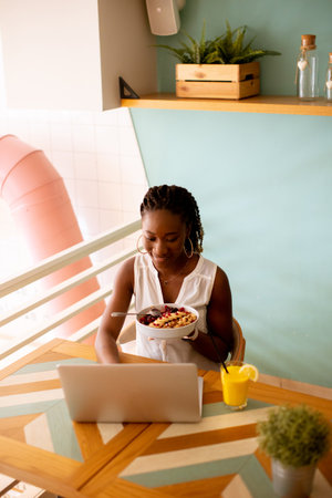 Pretty young black woman having a healthy breakfast while working on laptop in the cafe
