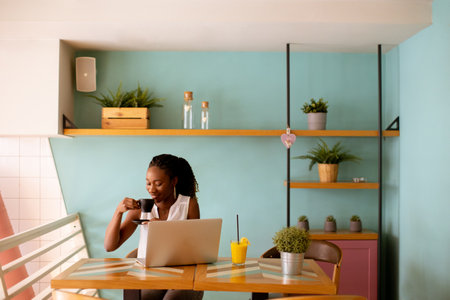 Pretty young black woman drinking coffee while working on laptop in the cafeの写真素材