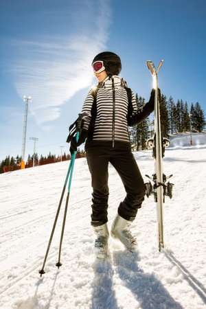 Young woman enjoying winter day of skiing on the snow covered slopes, surrounded by tall trees and dressed for cold temperaturesの写真素材