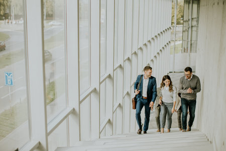 Group of corporate business professionals climbing at stairs in office corridor on a sunny dayの写真素材