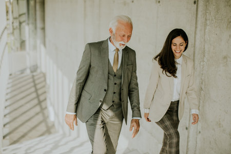 Handsome senior corporate business professional and his young female colleague climbing at stairs in office corridorの写真素材