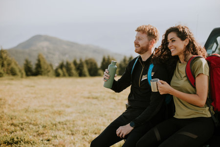Smiling young couple preparing hiking adventure with backpacks by terrain vehicleの写真素材
