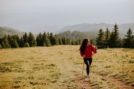Smiling young woman walking with backpack over green hillsの写真素材