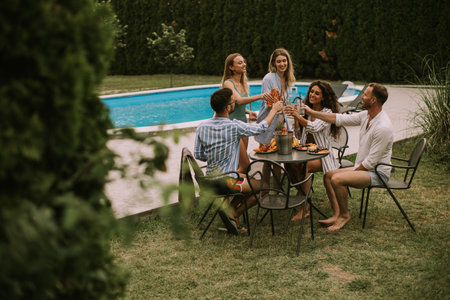 Group of happy young people cheering with cider by the pool in the gardenの写真素材