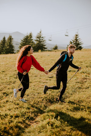 Smiling young couple walking with backpack over green hillsの写真素材