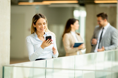 Young business woman standing with mobile phone in the office hallwayの写真素材