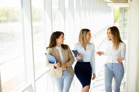 Three cute young business women walking on stairs in the office hallwayの写真素材
