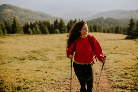 Smiling young woman walking with backpack over green hillsの写真素材